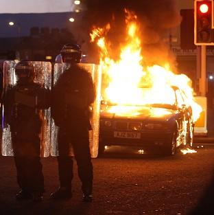Riot police stand next to a burned out car after loyalist protesters attacked police lines in east Belfast