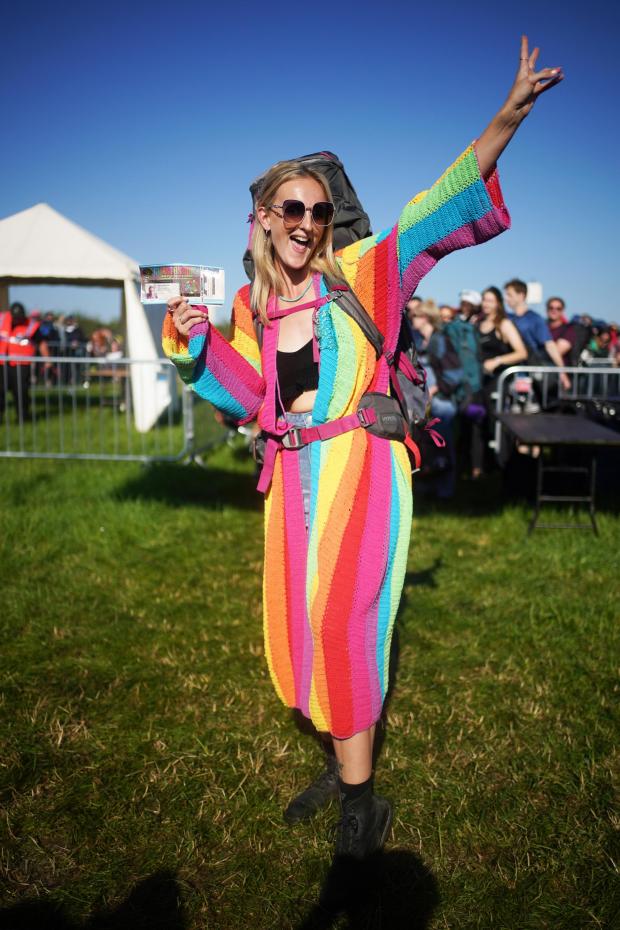 Somerset County Gazette: A colourfully dressed festivalgoer holds her ticket aloft at one of the festival's entrance points. Picture: Yui Mok, PA Wire